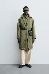 Trench color verde oliva de tejido técnico, corte relaxed fit, cuello solapa, manga larga, bolsillos laterales y abertura en la espalda.