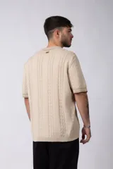 Camisa tejida color crudo, de manga corta, con cuello bowling y botones frontales. Presenta un tejido con textura de trenzas verticales y rib negro en los puños.