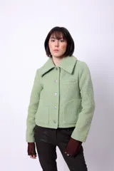 Campera corta de poliéster texturizado color verde oscuro, con cuello camisero, cierre frontal con botones a presión, bolsillos delanteros y forro interior. Incluye pins decorativos.