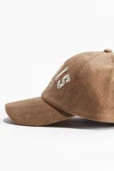 Gorra de béisbol color beige confeccionada en pana de algodón. Presenta bordado frontal con la leyenda "Paris Sports Club 1972" en color blanco.