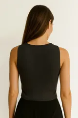 Top sin mangas color negro, ajustado al cuerpo, con cuello redondo y tres recortes circulares (cut-outs) verticales en el centro del pecho.
