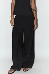 Pantalón palazzo negro de tejido fluido con tiro medio, cintura elástica en la espalda, bolsillos laterales ocultos y pinzas en el delantero.