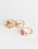 Set de tres anillos dorados de metal con diferentes diseños: uno con un corazón rosa, otro con forma de rosa y otro con una perla sintética.
