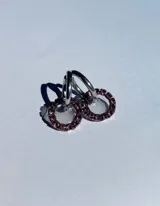 Par de aros colgantes con argollas doradas y dijes circulares de resina transparente con incrustaciones de strass de colores. El dije mide aproximadamente 1.5cm de diámetro.