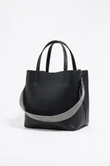 Bolso tote negro de cuero vacuno con doble asa corta y correa de tela extraíble. Interior con tres compartimentos y bolsillo con cremallera. Logo metálico de la marca en el frente.