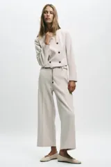 Blazer corta negra de cuello redondo y manga larga, con cierre frontal cruzado con botones dorados y falsos bolsillos delanteros.