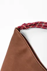 Bolso marrón con forma de media luna y asa de soga trenzada en rojo y blanco.
