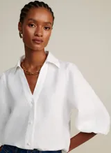 Camisa blanca de lino con cuello alto, escote en V, mangas 3/4 con volumen abullonado y puños elásticos.