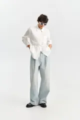 Camisa blanca de manga larga con cuello camisero, bolsillo frontal superior y tiritas ajustables en los costados para atar en la cintura.