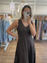 Vestido largo sin mangas, color marrón oscuro, con escote en V y corte amplio que cae hasta el tobillo. El ruedo tiene un acabado deshilachado.