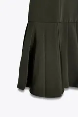 Vestido corto negro sin mangas, con cuello redondo y falda con tablas. Cierre trasero con cremallera oculta.