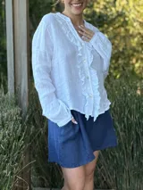 Camisa blanca de lino con cuello mao, mangas largas abullonadas y cierre frontal con botones de nácar. Presenta volados en el frente y puños elásticos.