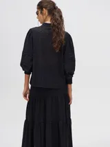 Camisa de broderie de algodón color negro, con cuello mao y cierre de cuatro botones. Presenta mangas abullonadas y galones con transparencias en la parte delantera y mangas.