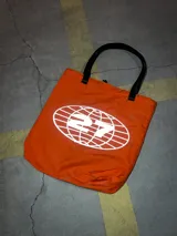 Conjunto puffer naranja con estampado del logo de la marca en negro. Incluye campera sin mangas con mangas desmontables, pantalón de jogging, gorro y tote bag. Resistente al agua y al frío.