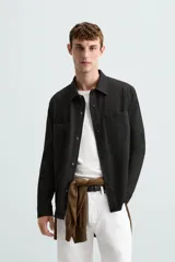 Sobrecamisa negra de tejido con elasticidad, cuello solapa, manga larga con puño abotonado, bolsillos de plastrón en el pecho y cierre frontal con botones a presión.