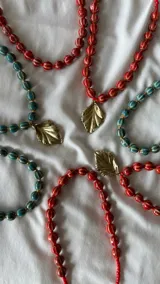 Collar corto de cuentas rojas con líneas horizontales blancas y cadena plateada para regular el largo.