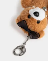 Llavero con dije de oso de peluche color marrón claro, con moño negro, collar de perlas y dije de corazón plateado.