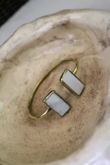 Pulsera rígida dorada con dos piedras rectangulares de color blanco nacarado en los extremos.