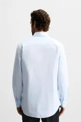 Camisa celeste a rayas verticales, de corte regular, confeccionada en algodón, con cuello italiano, manga larga con puños abotonados y cierre frontal con botones.