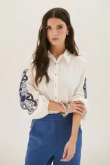 Camisa blanca de manga larga con bordados florales marrones en las mangas.