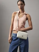 Cartera bandolera Calvin Klein color blanco, con correa ajustable, cierre de cremallera y logo CK metálico en el frente.