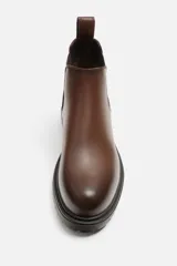 Bota Chelsea de cuero color marrón con elástico lateral y tirador trasero. Suela track de goma negra.