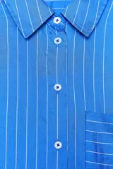 Camisa celeste con rayas verticales blancas, de corte oversize, cuello solapa, manga larga con puños y bolsillo de plastrón en el pecho.
