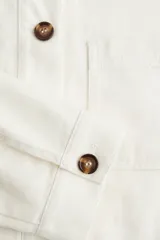Campera color crudo en sarga de algodón con cuello, botones adelante y canesú en la espalda. Modelo de hombros apenas caídos con bolsillos superiores de parche, bolsillos insertados adelante y puños abotonados.