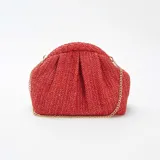 Bolso de mano tipo clutch, color rojo, confeccionado en rafia trenzada. Tiene forma rectangular con pliegues en la parte superior y cierre con broche imantado. Incluye una cadena dorada para usar como bandolera.