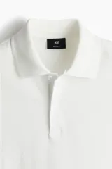 Remera polo blanca de piqué de algodón, corte regular fit, con cuello clásico, tapeta de botones, mangas cortas, remate acanalado en cuello y mangas, y bajo recto con aberturas laterales.
