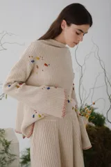 Sweater beige de lana con cuello redondo y mangas largas. Presenta detalles de bichos tejidos a contratono en la parte superior delantera.