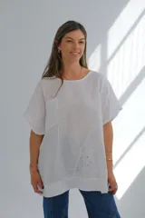 Blusa blanca de lino con cuello redondo, mangas cortas, bolsillo en el pecho y detalle de bordado calado en el lateral inferior. Corte holgado.