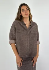 Chaqueta color gris con textura, de corte recto, cuello camisero, cierre frontal con botones, mangas 3/4 con puños arremangados, dos bolsillos de parche en el pecho y ruedo recto.
