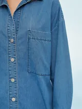 Camisa de jean celeste, de corte amplio, con cuello clásico, cierre frontal con botones y bolsillo de parche en el pecho.