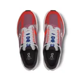 Championes de running On Cloudsurfer Next, color rojo y azul, con detalles en gris y blanco. Presentan tecnología CloudTec Phase para una amortiguación suave y reactiva.