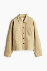 Campera color beige de sarga de algodón, con cuello, botones al frente y canesú en la espalda. Tiene hombros caídos, bolsillos superiores de parche, bolsillos insertados al frente y puños abotonados.