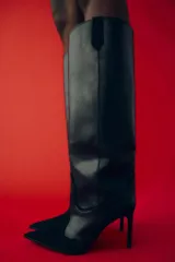 Bota alta de cuero negro con puntera fina y tacón de aguja. Diseño estilo cowboy con paneles combinados de cuero liso y gamuza.
