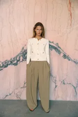 Chaqueta color crema de tejido de punto liso, con cuello redondo, manga larga, bolsillos delanteros de plastrón y cierre frontal con botones dorados.