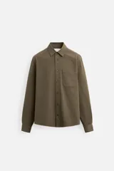 Camisa color verde oliva de corte relaxed fit, confeccionada en tejido de algodón con acabado cepillado. Tiene cuello solapa, manga larga con puño abotonado, bolsillo plastrón en el pecho, efecto lavado y cierre frontal con botones.