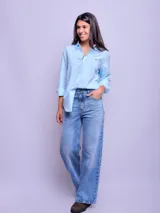 Camisa blanca de algodón, corte holgado, con cuello clásico y botones frontales. Las mangas son largas y se ven remangadas.