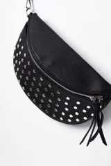Riñonera negra de cuero sintético con forma de media luna, cierre superior con doble cremallera y correa regulable con mosquetón. Decorada con tachas plateadas y flecos colgantes.