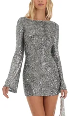 Vestido corto plateado de lentejuelas con mangas largas acampanadas y espalda descubierta que se ata con tiras.
