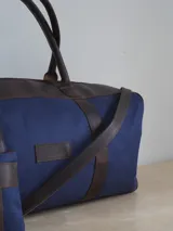 Bolso de lona azul con detalles en cuero marrón, doble asa de mano y correa bandolera ajustable. Incluye un neceser haciendo juego con cierre y logo de caballo bordado.