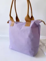 Bolso tipo tote de lona color fucsia con asas de cuero marrón, bolsillo interno y externo.