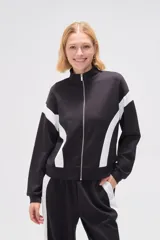 Campera deportiva negra con cierre frontal, cuello alto y detalles de recortes curvos blancos en mangas y laterales.