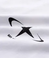 Remera blanca de algodón, corte oversized, con cuello redondo y mangas cortas. Presenta un estampado frontal con un ángel y el texto "PARADISE" en negro, y un pequeño gráfico de estrella/brújula en el lado izquierdo del pecho.