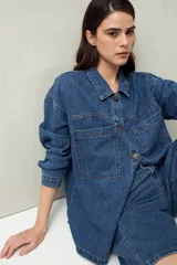 Sobrecamisa oversize de jean azul con cuello camisero, cierre frontal con botones, mangas largas y bolsillos de parche en el pecho.