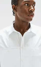 Camisa blanca de manga corta, corte oversize y confeccionada en poplin 100% algodón. Presenta dos bolsillos delanteros, uno con solapa y otro con ojal y botón.