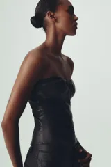 Top tipo corsé negro de cuero sintético, con escote corazón y hombros descubiertos. Detalle de costuras marcadas y cierre trasero con cremallera.