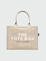 Bolso tipo tote color beige con bordes grises y estampado frontal con el texto "THE TOTE BAG MARC JACOBS" en blanco.